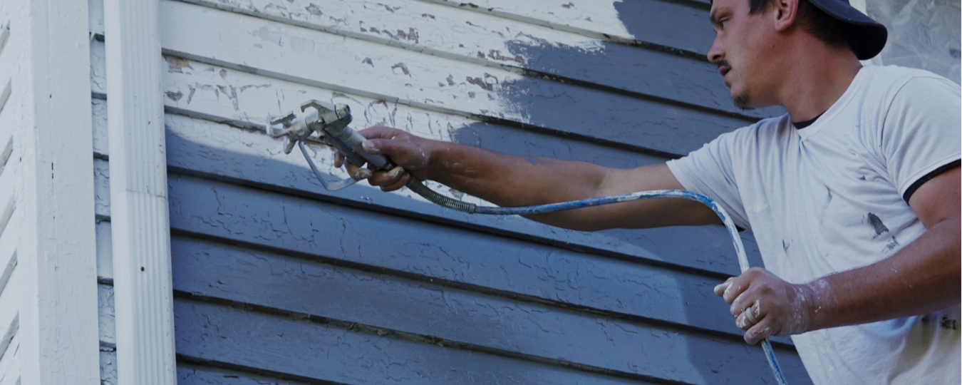 Person painting a house exterior with a paint sprayer